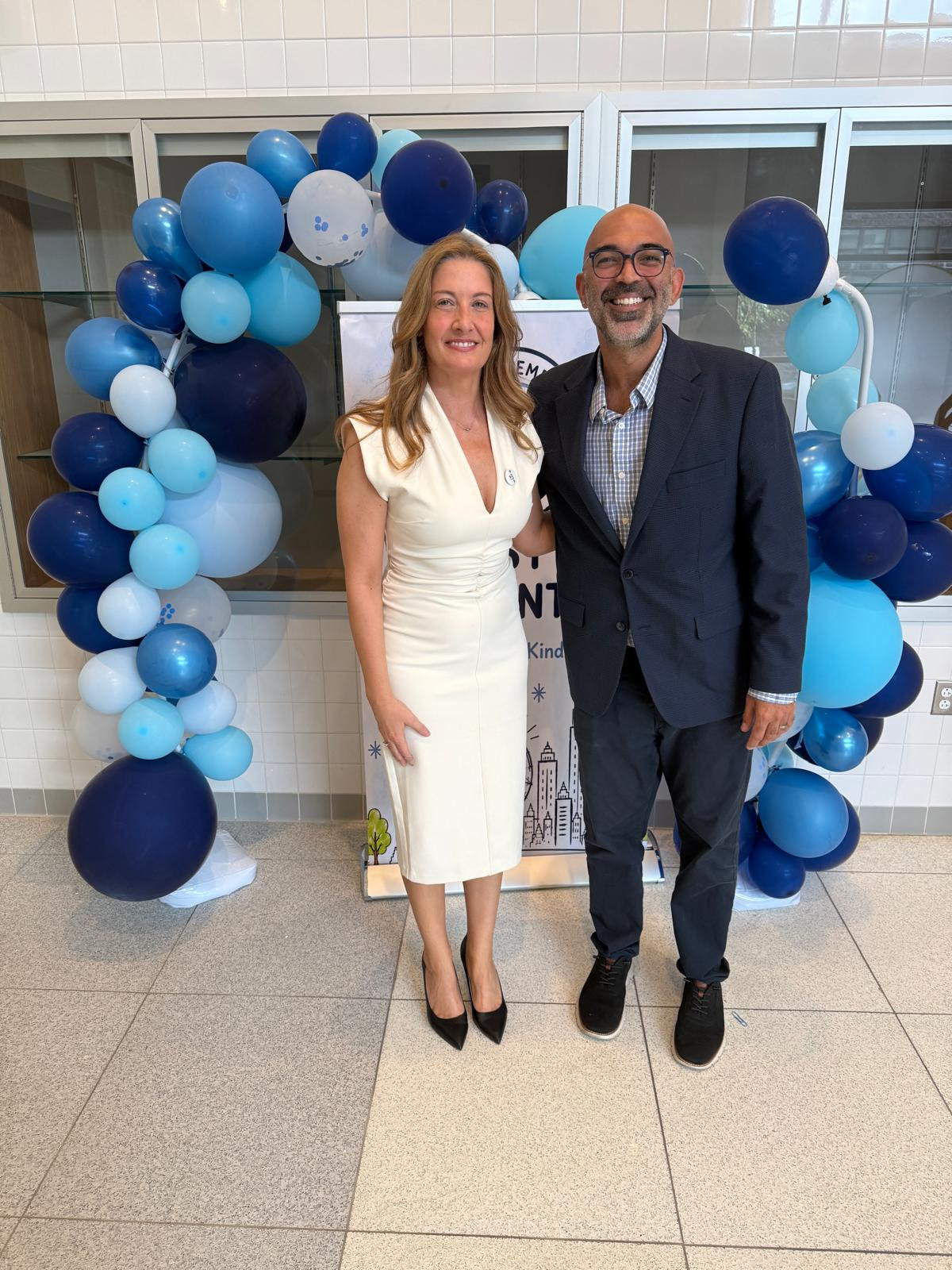 Two West Q educators smiling beside a navy and sky-blue balloon arch
